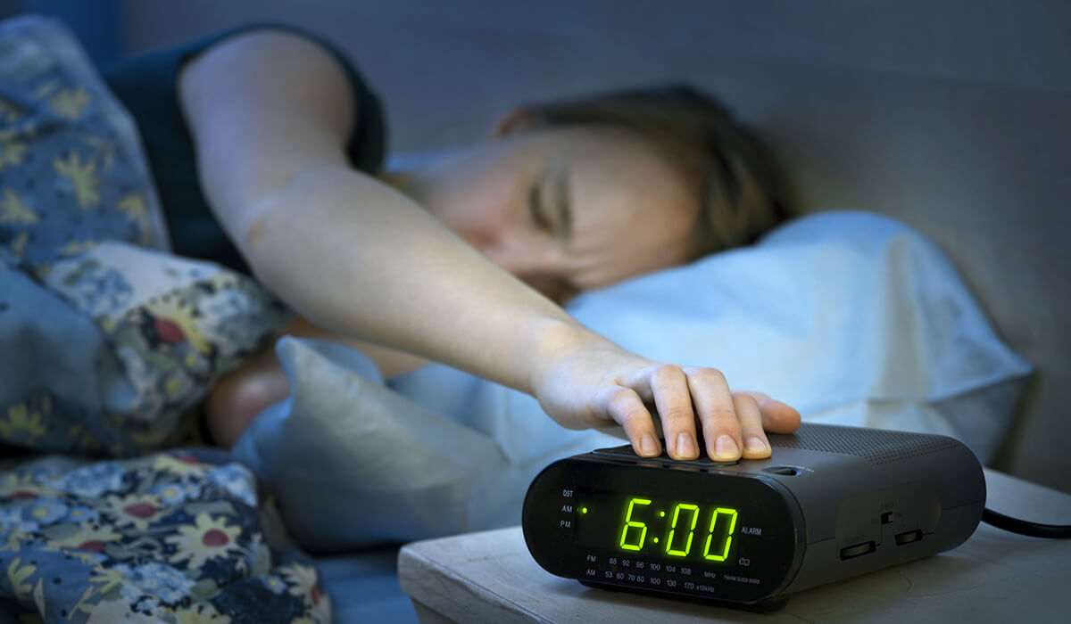 woman who wants to learn how to sleep better turns off her alarm clock