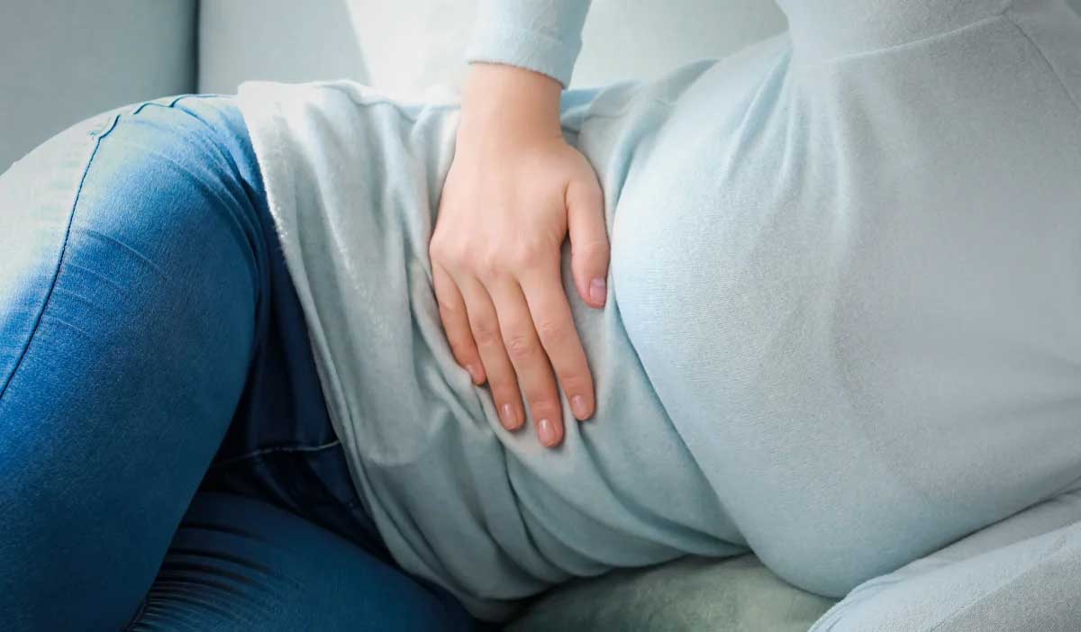 woman on a couch holding her abdomen because she is experiencing pain and other signs of appendicitis