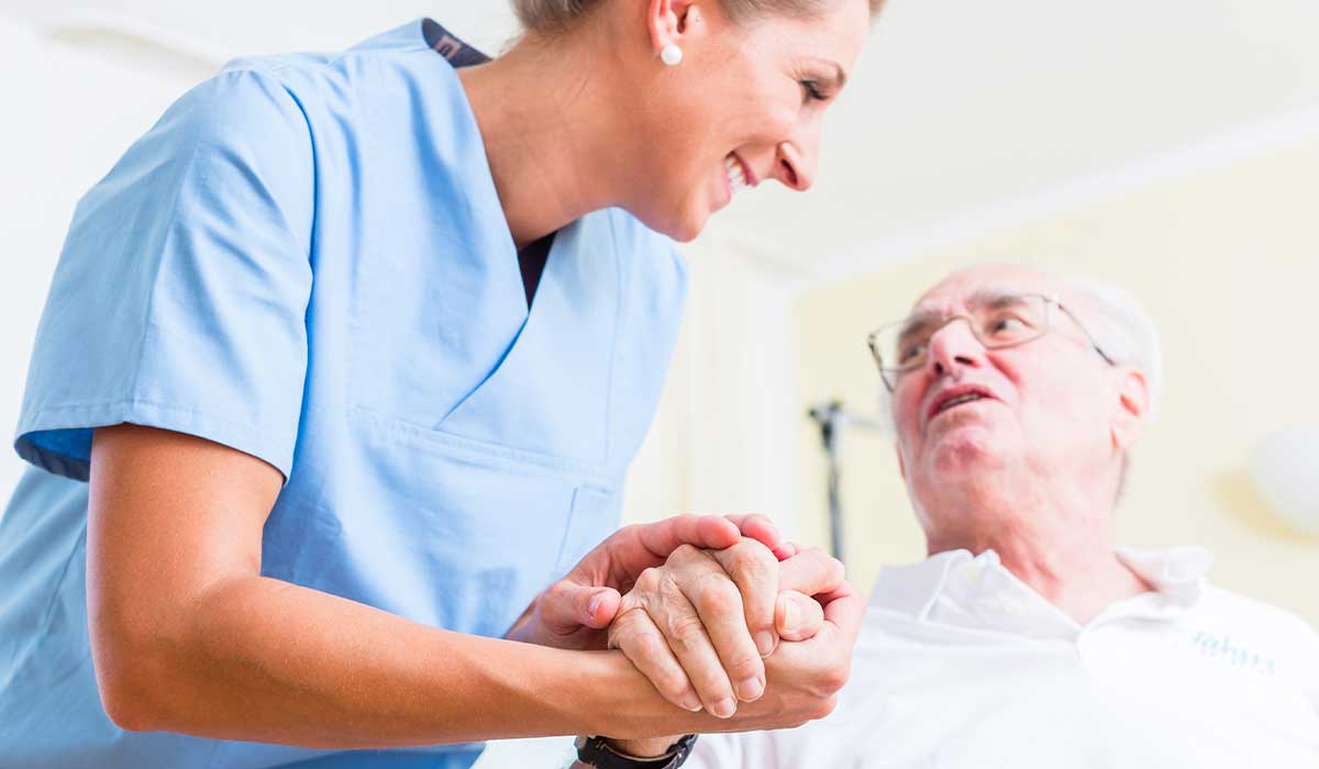 a nurse holds the hand of an elderly patient who is going to get a check for prostate cancer